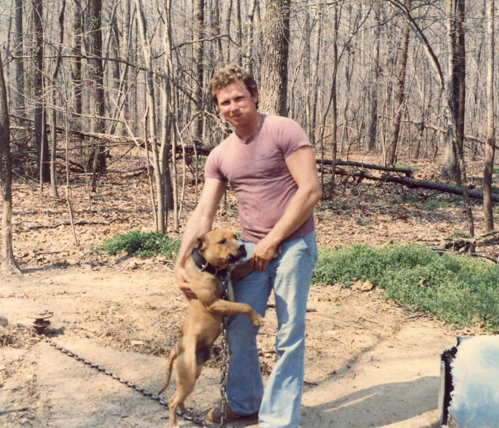 A man and his dog are standing in the woods.