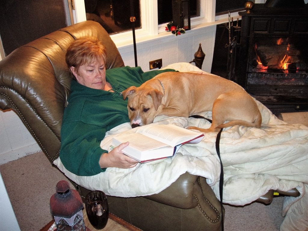 A woman and dog are laying in the chair reading.