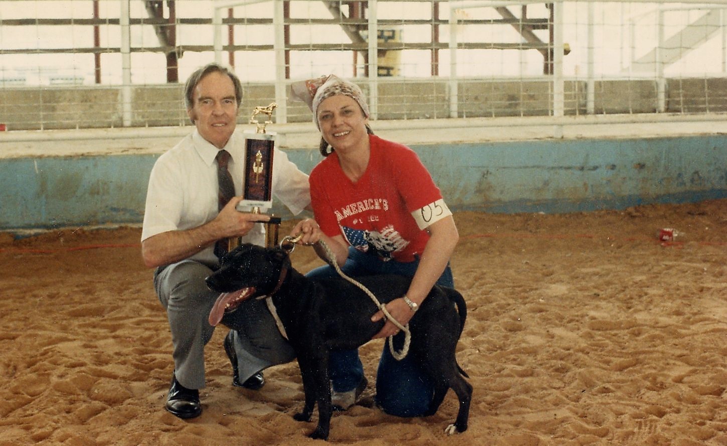 A man and woman holding a trophy with a dog.